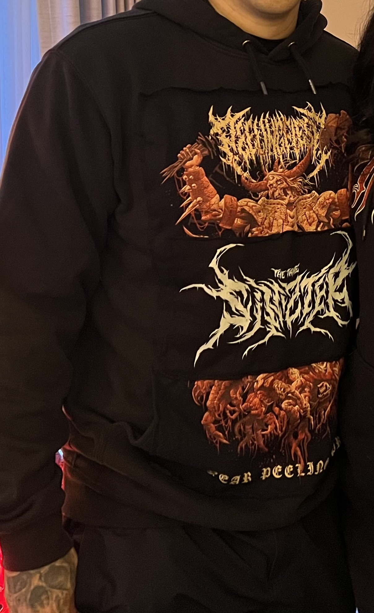 A person wearing a black hoodie with intricate graphic designs featuring various colorful images and text.