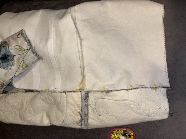 A close-up view of fabric pieces laid out for sewing, with white and patterned textiles pinned together, showcasing frayed edges and stitching details.