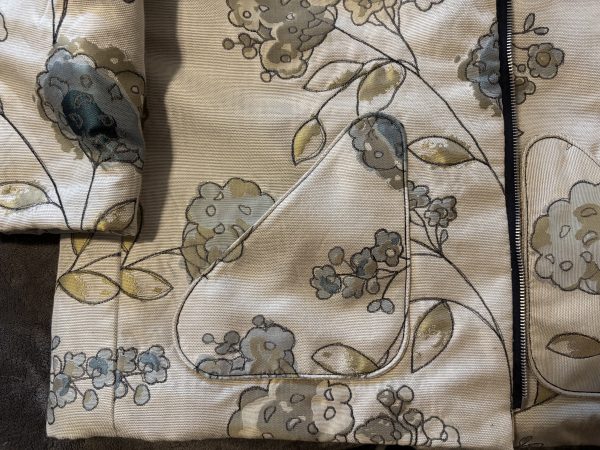 Close-up of a floral patterned fabric featuring intricate designs in shades of blue, beige, and green, highlighting a triangular patch on a jacket.