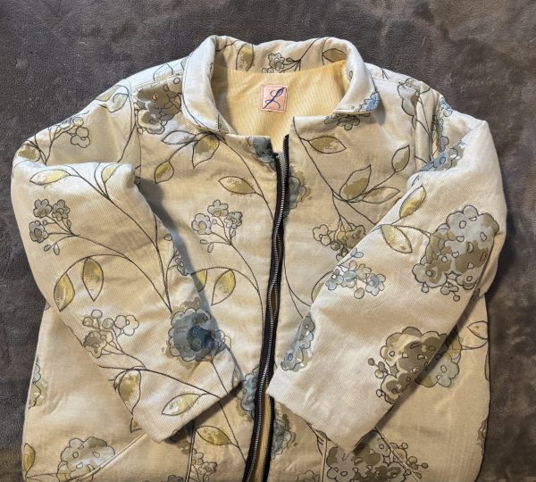 A soft, flower-patterned baby jacket with a zip closure, featuring shades of blue and yellow on a cream background.